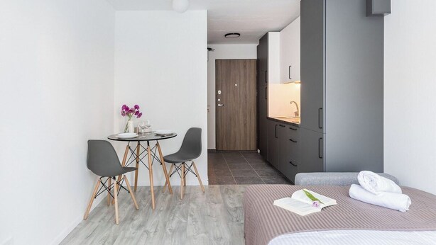 A modern hotel room with a bed, a small dining table with chairs, a kitchenette, and a bathroom. - River to the City Self check in (Vilnius)