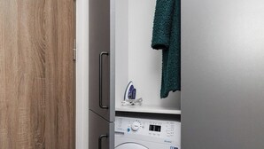 A compact, modern laundry room with a built-in washing machine and dryer, a wooden cabinet, and a towel hanging on the wall.