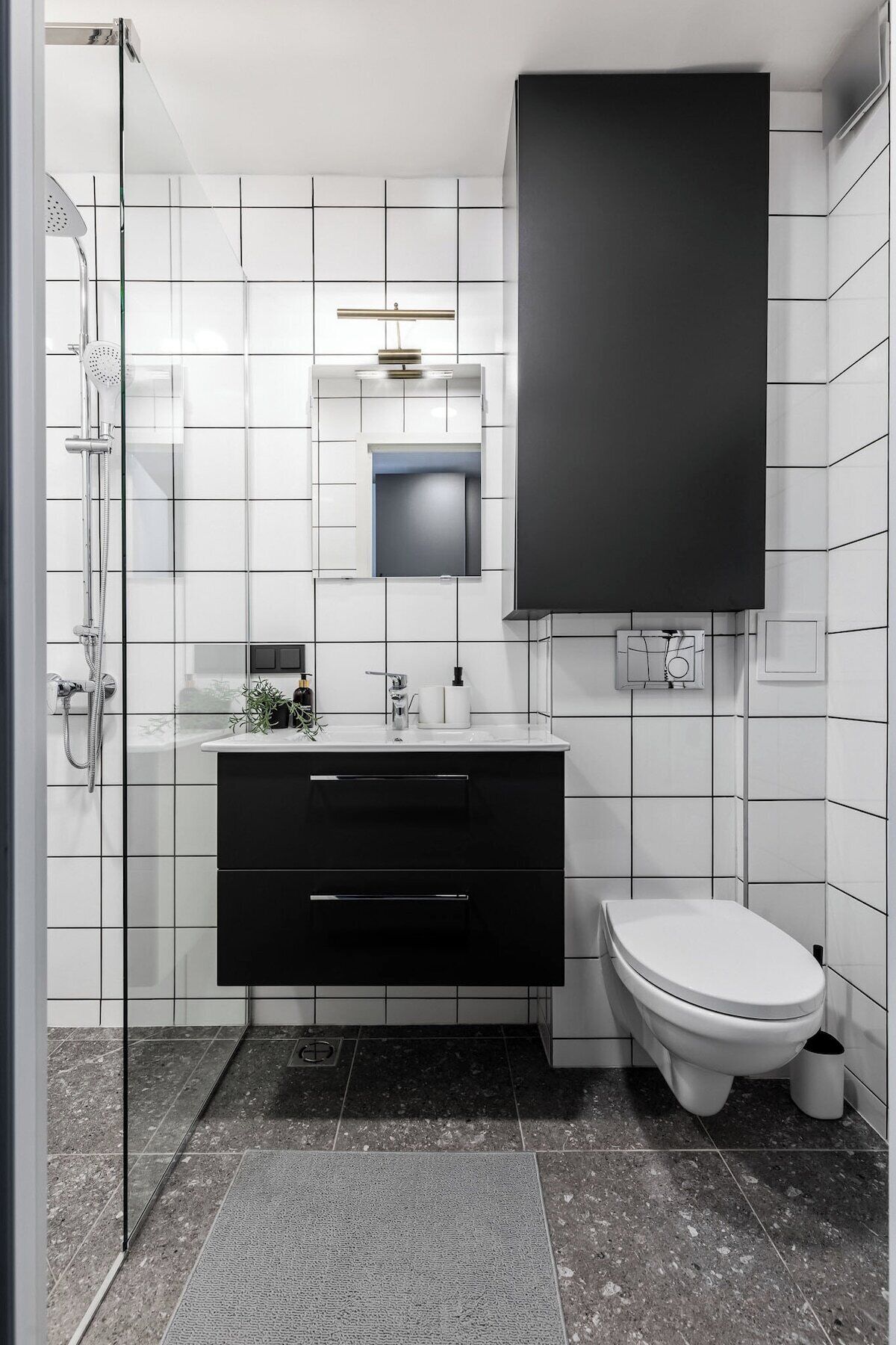 A modern bathroom with a black vanity, white tiles, a glass shower enclosure, and a toilet.