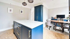A modern kitchen with a central island, blue cabinetry, and a dining area with a wooden table and chairs. - Charming Two-Bedroom Home in London (Greater London)