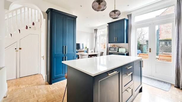 A modern kitchen with blue cabinets, a white island, and pendant lighting. - Charming Two-Bedroom Home in London (Greater London)