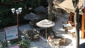 An outdoor restaurant area with tables, chairs, and thatched umbrellas. - Cozy 2 Bedroom Cabin Sleeps 5 in Lido di Spina, Italy - Perfect Family Retreat (Comacchio)