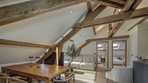Ein Schlafzimmer im Loft-Stil mit schrägem Dach, Holzbalken, einem Bett und Blick ins Freie.
