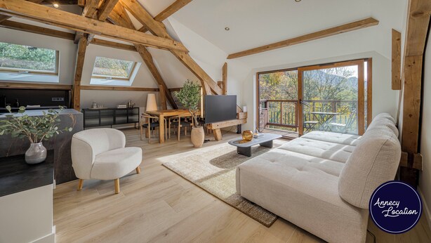 Ein gro ßzügiger Loft-Wohnbereich mit freiliegenden Holzbalken, einem großen Fenster mit Blick ins Freie, einer bequemen Couch und einem Essbereich mit Fernseher.