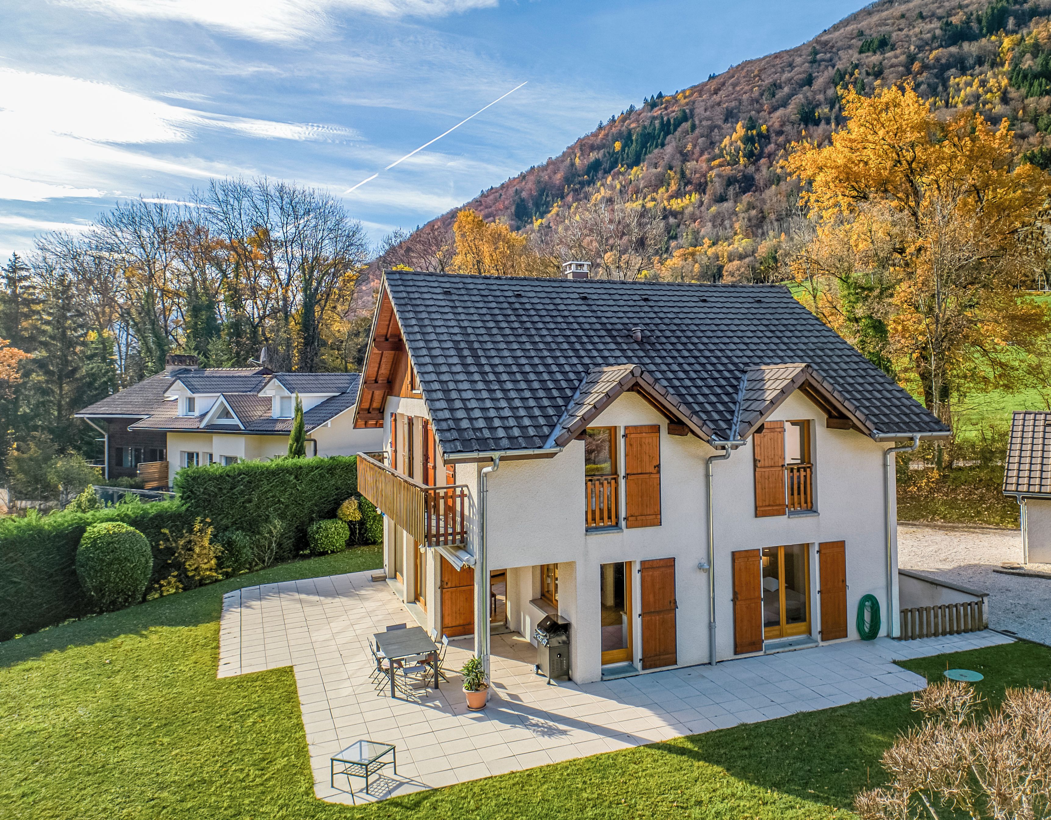 Ein zweistöckiges Haus mit Ziegeldach, einem Balkon und einer gepflasterten Terrasse.