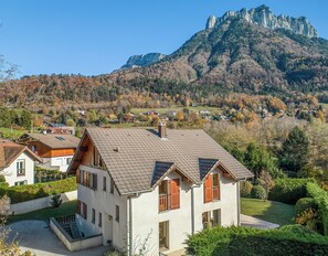 Ein zweigeschossiges Haus mit geneigtem Dach, Holzhörnern und einer sichtbaren Treppe zum Eingang.