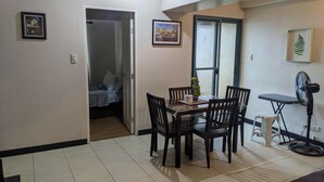A dining area with a table and chairs, a small fan, and a window with a view. - Splendid 2 Bedroom in Tivoli Garden Residences, high floor, spacious, balcony (Mandaluyong City)