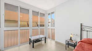 Ein Schlafzimmer mit einem Bett, einem Nachttisch mit Lampe, einem kleinen Tisch und einem Fenster mit Jalousien.