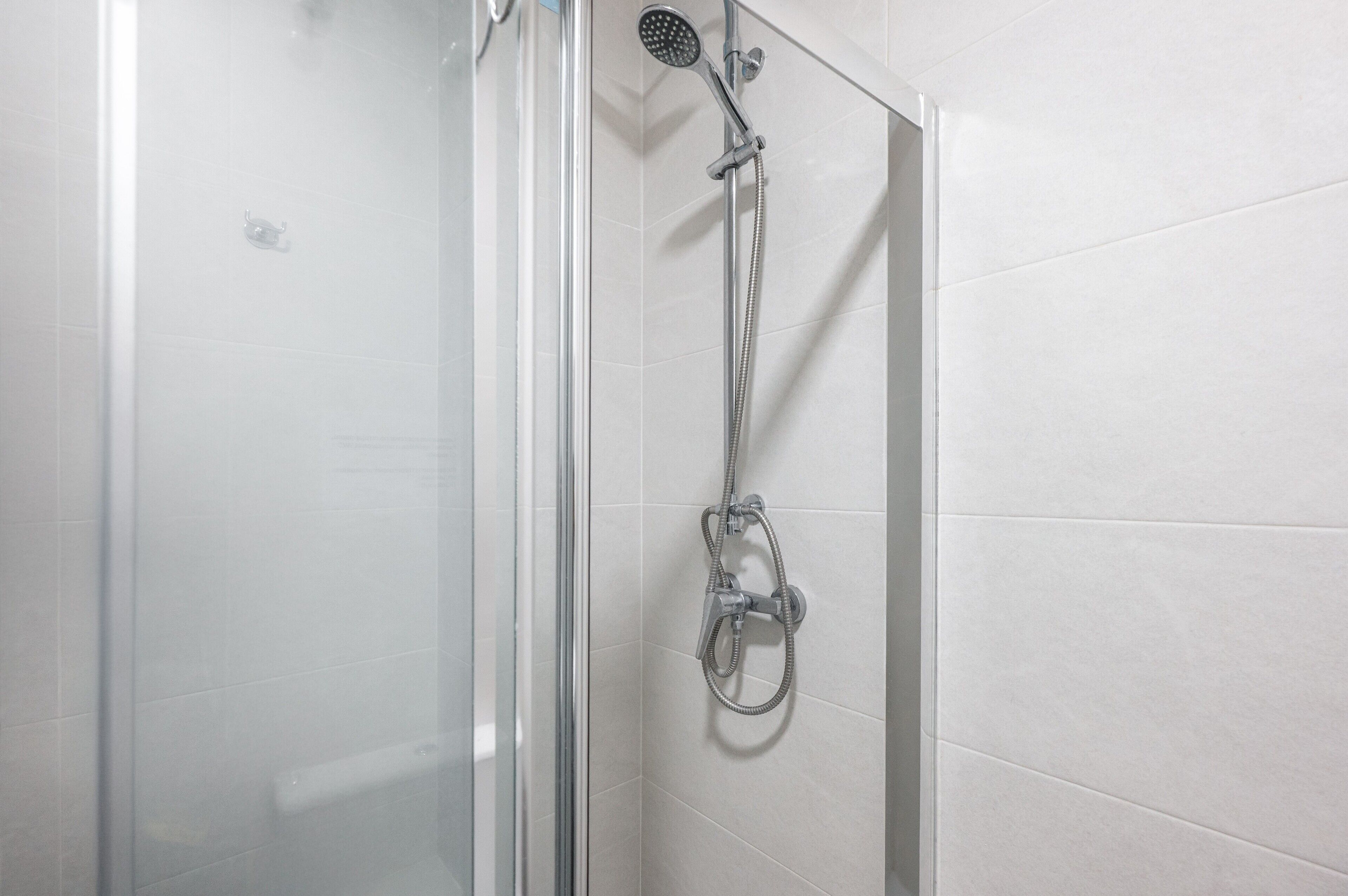 A glass-enclosed shower with a handheld showerhead and a wall-mounted faucet.