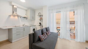 Ein kompakter Wohnraum mit Küchenzeile, einer Couch mit Zierkissen und einem Balkon mit Blick.