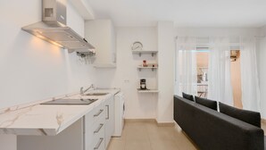 Eine moderne Küche mit weißen Schränken, einem eingebauten Herd und einem Essbereich mit einem dunkelgrauen Sofa und Vorhängen.