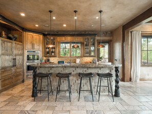 A spacious kitchen with wooden cabinets, a granite countertop, and three bar stools.
