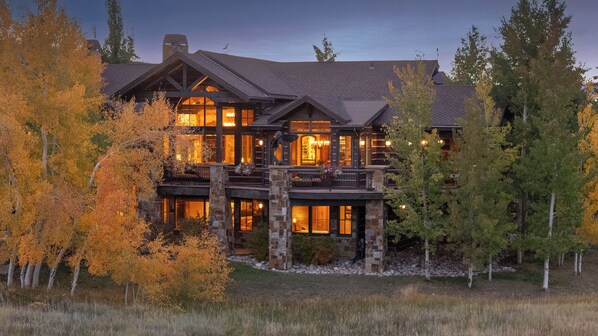 A large, multi-story log cabin with a prominent balcony and stone foundation.