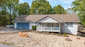 A single-story house with a front porch, a garage, and a gravel driveway.