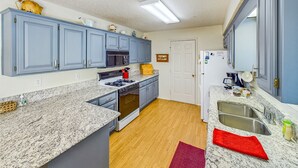 A kitchen with blue cabinets, a granite countertop, a stove, a microwave, and a refrigerator.