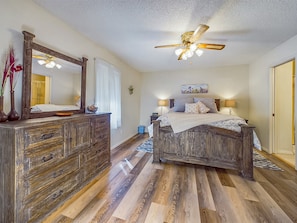 A bedroom with a wooden bed, a dresser, a ceiling fan, and a large mirror.