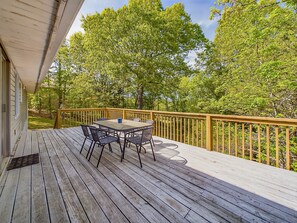 Een houten terras met een tafel en stoelen, omringd door een houten balustrade en bomen.