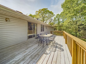 A wooden deck with a table and chairs, a sliding glass door, and a view of trees.