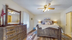 A bedroom with a wooden bed, a dresser, a ceiling fan, and a large mirror.