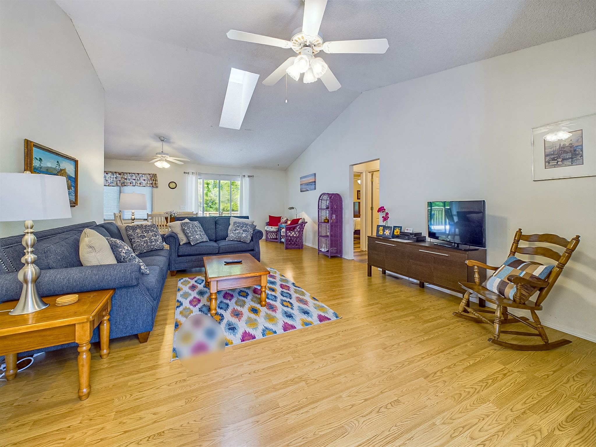 A spacious living room with a ceiling fan, a sofa set, a coffee table, a TV, and a rocking chair.