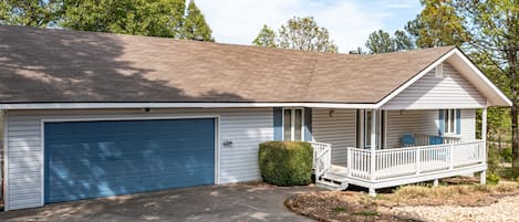 Une maison de plain-pied avec une porte de garage bleue, un porche couvert avec une balustrade blanche et un petit arbuste vert devant.