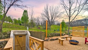 Ein rustikaler Außenbereich mit einer Holzhütte mit dem Schild 'BATHROOM', Holzbanken und einem Picknicktisch.