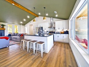 Una cocina moderna con armarios blancos, una isla central con taburetes y un ventanal grande.