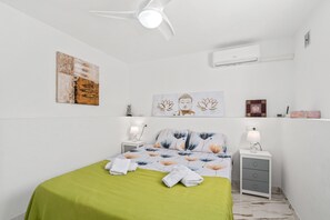 A bedroom with a bed, two bedside tables, a ceiling fan, wall art, and an air conditioning unit.