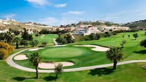 Ein Golfplatz mit Sandbunkern, einem Fußweg und Gebäuden im Hintergrund.