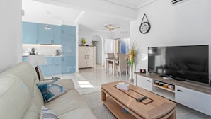 Ein modernes Wohnzimmer mit Sofa, Couchtisch, Fernseher und einer Küche im Hintergrund.