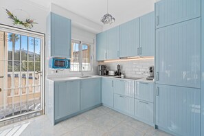 A kitchen with light blue cabinets, a microwave, a sink, and a window with a view.