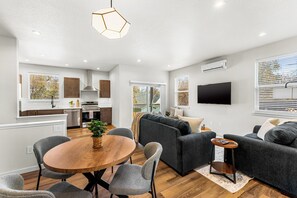 Ein modernes Wohnzimmer mit einem grauen Sofa, einem Holzesstisch und einem an der Wand montierten Fernseher.