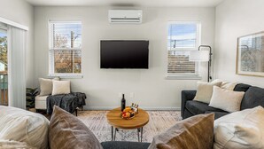 Egy modern nappali, melyben egy síkképernyős televízió, egy kerek, fából készült dohányasztal és egy kanapé található.