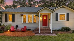 A two-story house with a red door, a front porch with red chairs, and a small garden area. - Belote Place Bungalow (Jacksonville)