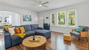 A living room with a sectional sofa, a round coffee table, a rattan chair, and a ceiling fan. - Belote Place Bungalow (Jacksonville)