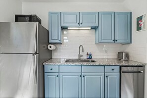 Una cocina con un refrigerador de acero inoxidable, un microondas, un fregadero con grifo y armarios azules.