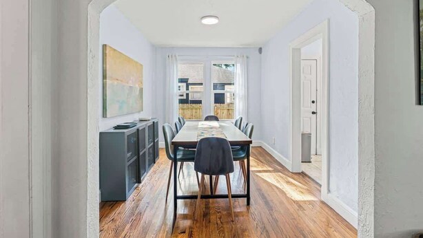 A dining area with a long table, chairs, and a kitchen area with cabinets and a refrigerator. - Belote Place Bungalow (Jacksonville)