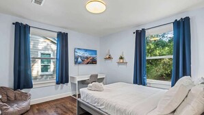 A bedroom with a bed, a desk, a chair, a sofa, and a window with curtains. - Belote Place Bungalow (Jacksonville)