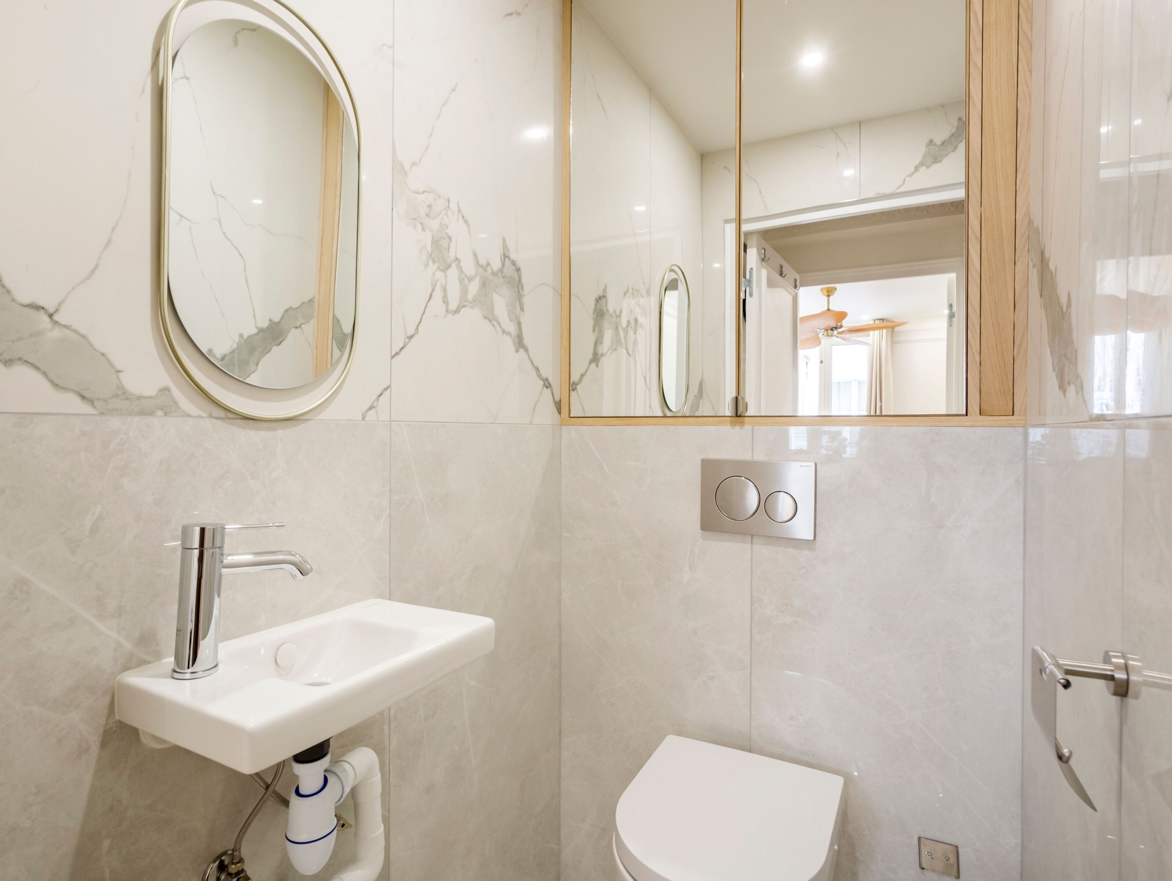 A modern bathroom with a marble wall, a sink, a toilet, and a mirror.