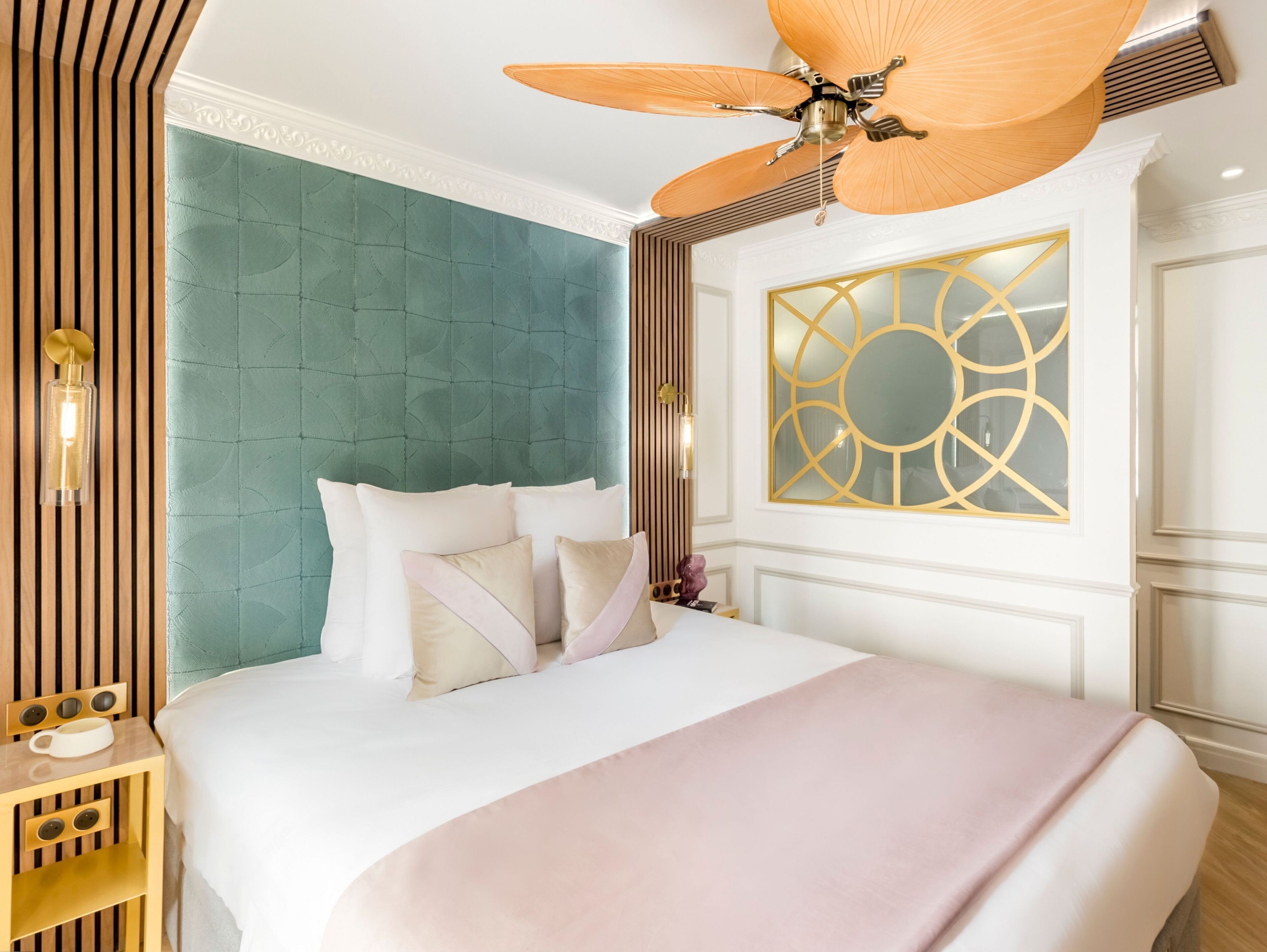 A hotel room with a large bed, a ceiling fan, a decorative wall panel, and a nightstand with a lamp.