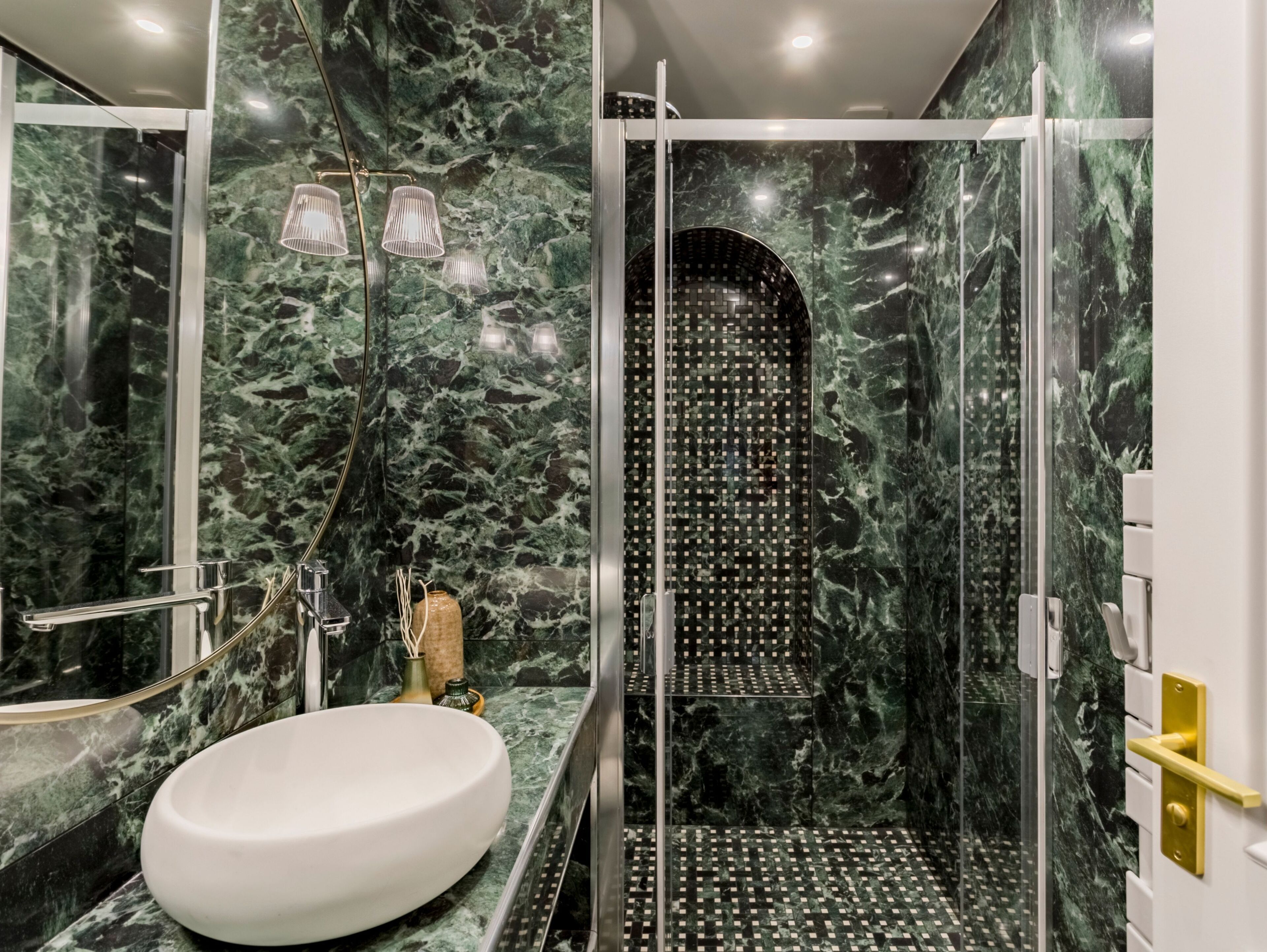 A modern bathroom with a white sink, a glass shower enclosure, and marble walls.