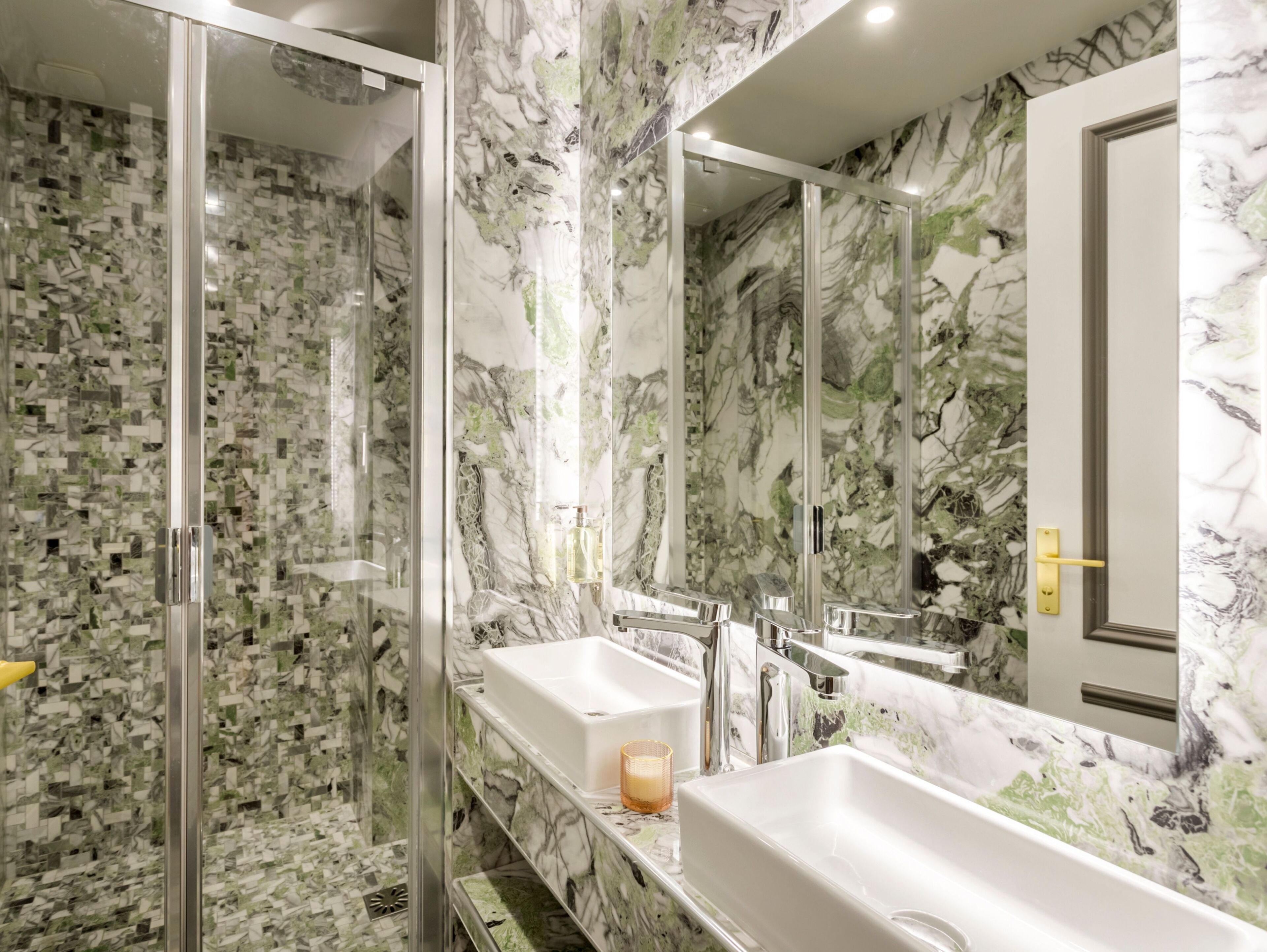 A bathroom with two sinks, a glass shower enclosure, and a marble backsplash.