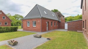 Een gebouw van rode bakstenen met een schuin dak, een verharde oprit en een kleine tuin.