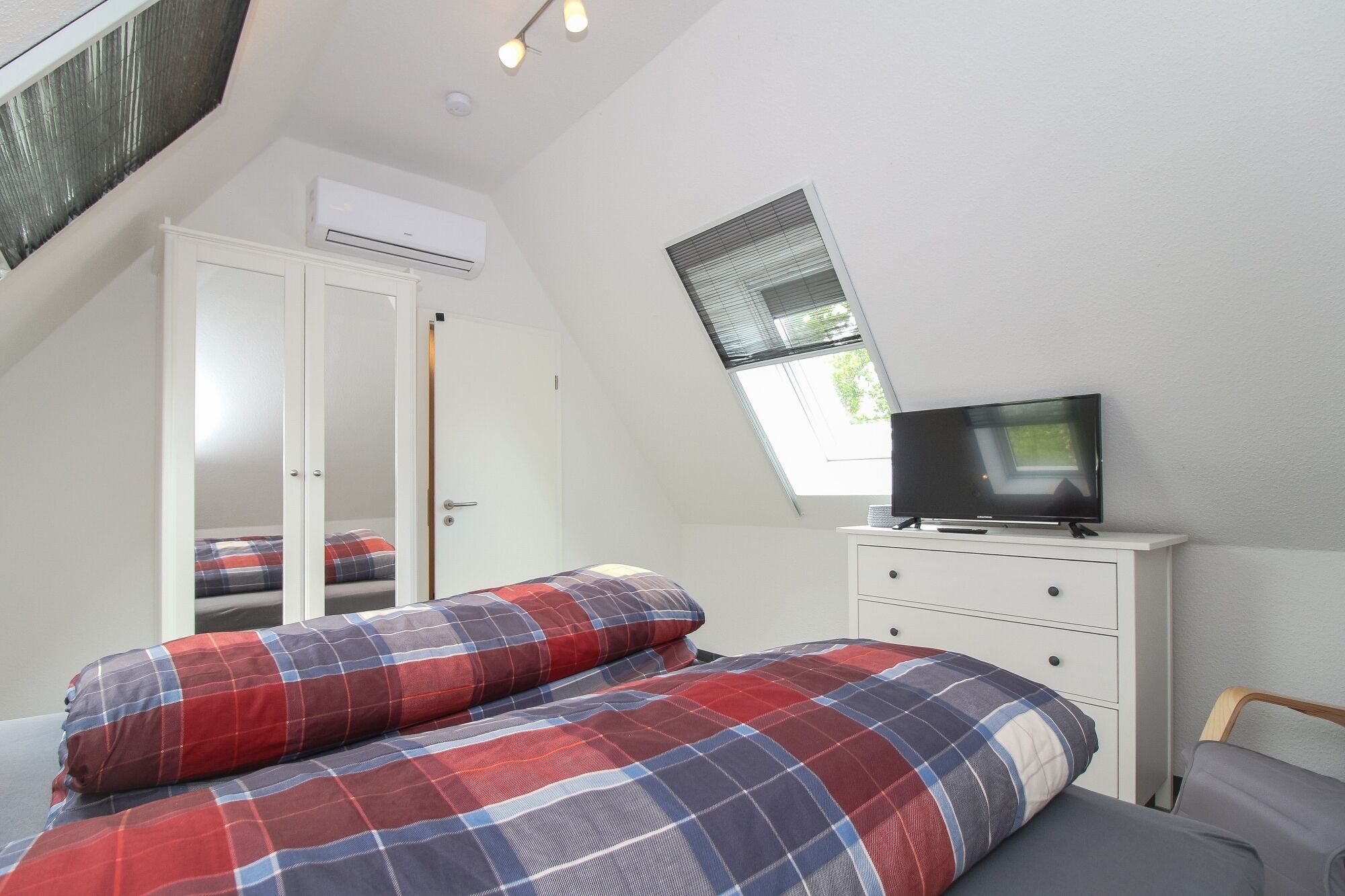 Une chambre à coucher avec un lit, un téléviseur posé sur une commode, une armoire et un puits de lumière.