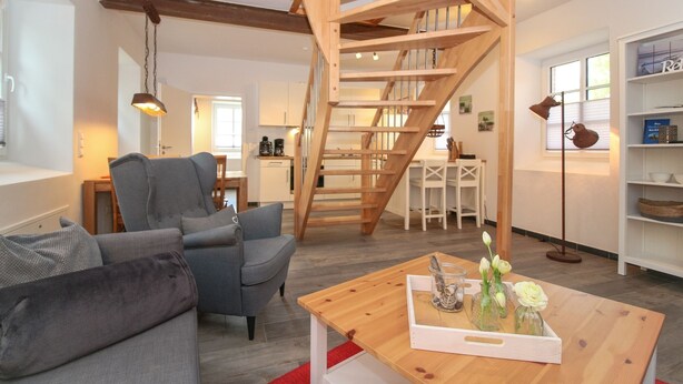 Een gezellige woonkamer met een grijze bank, een houten salontafel en een houten trap.