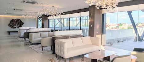 A modern hotel lobby with a sofa, chairs, a coffee table, and a large window offering a city view.