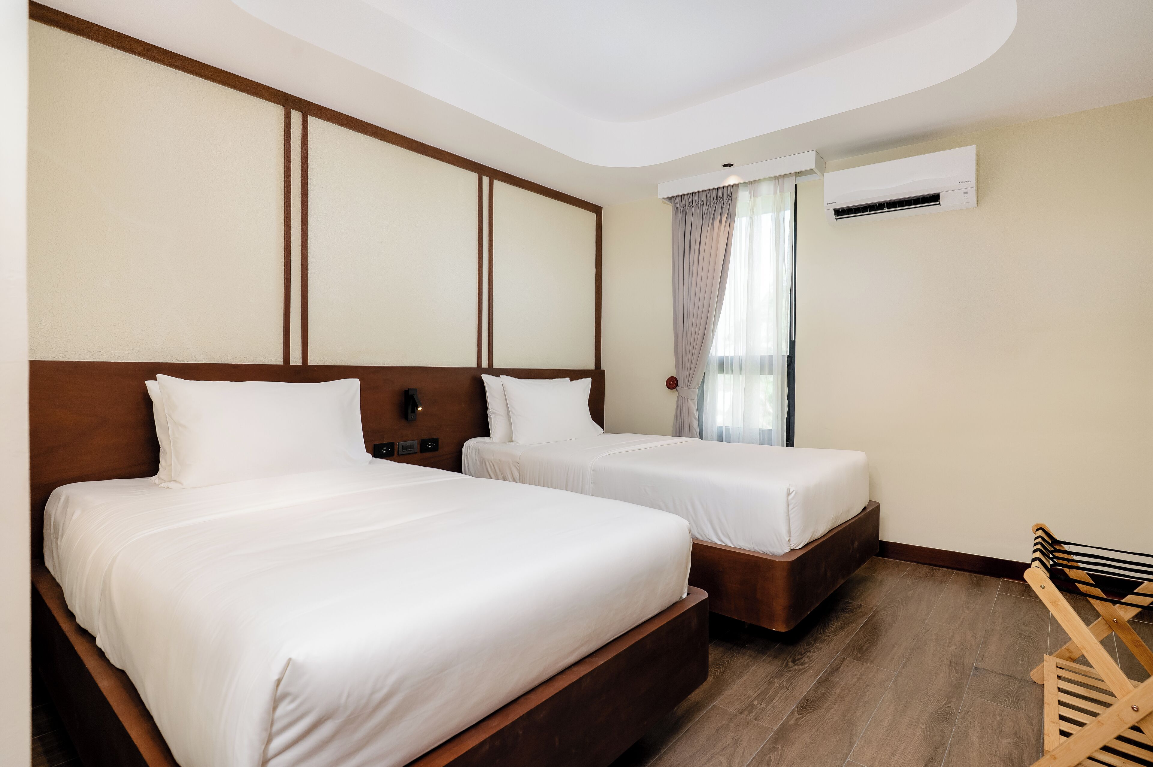 Habitación de hotel con dos camas, cabeceros de madera, un banco de madera y un equipo de aire acondicionado.