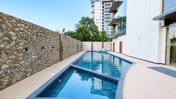 Una piscina con un muro de piedra en un lateral y un edificio moderno al fondo.