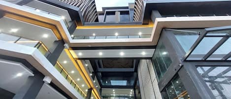 Ein modernes, mehrstöckiges Gebäude mit einem zentralen Atrium, Glasgeländern und einer geometrischen Fassade.