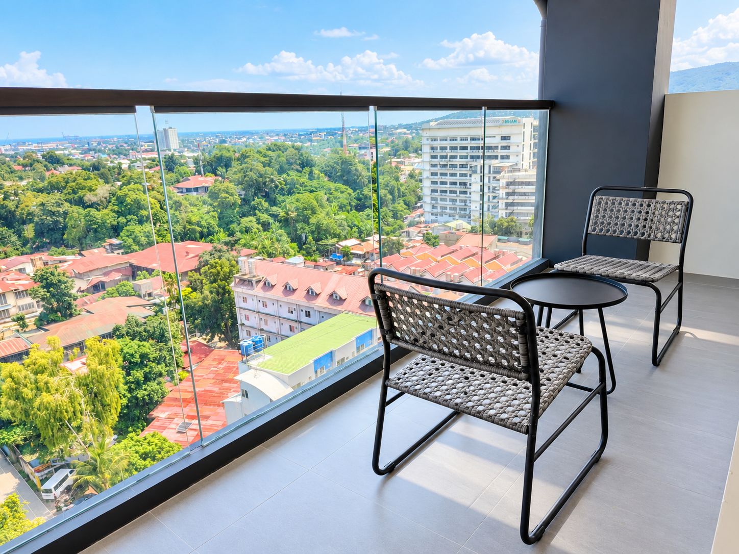A balcony with a view of a cityscape, two wicker chairs, and a small table.